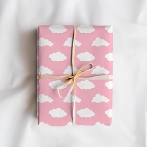 May include: A wrapped gift with a pink background and a pattern of white clouds. The gift is tied with a beige ribbon, creating a soft and whimsical aesthetic. The wrapping paper is a light pink color.