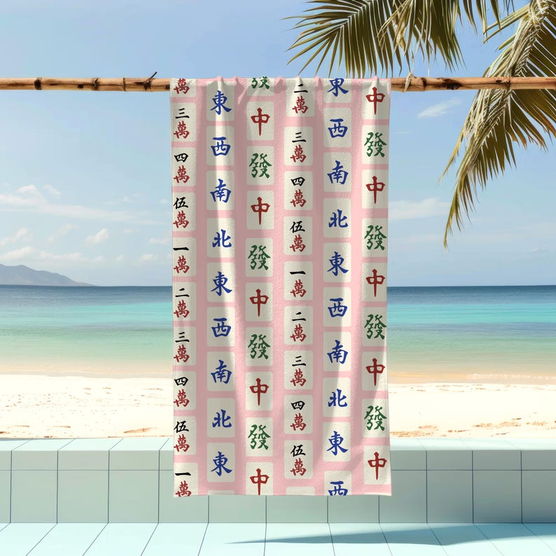 Może przedstawiać: R&oacute;żowy ręcznik plażowy z powtarzającym się wzorem chińskich kostek mahjong. Kostki przedstawiają znaki dla Wschodu, Południa, Zachodu, P&oacute;łnocy, Wiatru, Smoka i Bambusa.