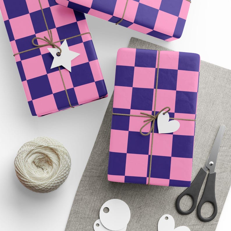 May include: Overhead view of wrapped presents with a pink and purple chequered pattern. Each gift is tied with twine and a white paper tag. A ball of twine, scissors, and blank tags are also visible.