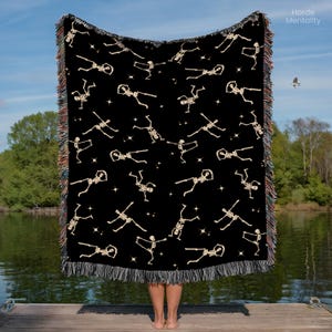 May include: Black woven throw blanket featuring a repeating pattern of beige skeletons and stars. The blanket has a fringed edge with a mix of colors. The words "Horde Mentality" are in the upper right corner.