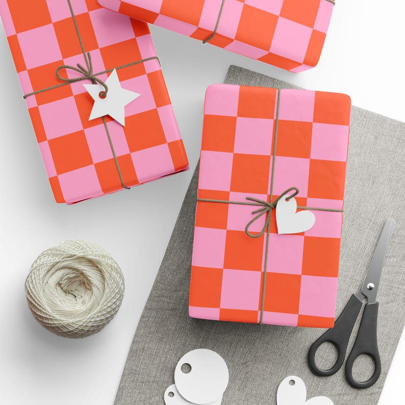 May include: Overhead view of wrapped presents with a pink and orange chequered pattern. Each gift is tied with twine and a white paper tag. A ball of twine, scissors, and blank tags are also visible.