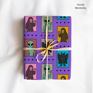 May include: A wrapped gift with purple wrapping paper featuring cartoon illustrations of aliens, Bigfoot, and a mothman. The gift is tied with a cream-colored ribbon. The text "Horde Mentality" is visible.