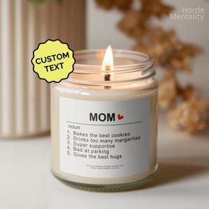 Puede incluir: Una vela encendida en un frasco de vidrio transparente con una etiqueta blanca. La etiqueta dice "MOM" con una definición que incluye "Bakes the best cookies" y "Gives the best hugs". Una pegatina amarilla con "CUSTOM TEXT" está en la imagen.