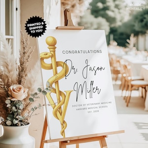 May include: A white graduation sign on an easel with the text "Congratulations Dr. Jason Miller" in black script. A gold medical symbol is featured. The sign also includes "Doctor of Veterinary Medicine, Harvard Medical School, Est. 2026."