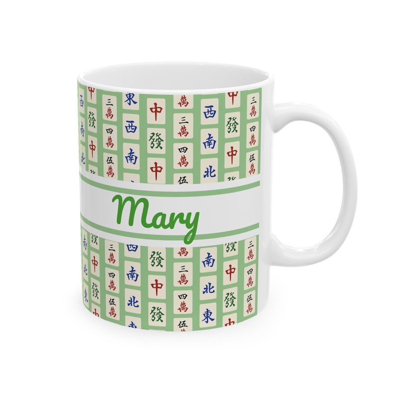 May include: White ceramic mug featuring a green and white design with Mahjong tiles and the name "Mary" in green script. The mug has a white handle and a light green band with the name.