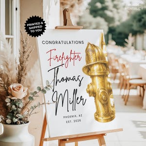 以下が含まれることがあります： イーゼルに立てられた白い看板。黒と赤の筆記体で「Congratulations Firefighter Thomas Miller」と書かれています。右側には金色の消火栓とヘルメットのイラスト。看板はPhoenix, AZ, EST. 2026用です。