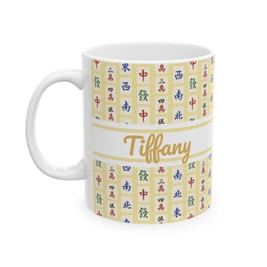 May include: White ceramic mug with a handle, featuring a design of Chinese characters and the name "Tiffany" in gold script. The mug has a cream-colored background with a pattern of red, green, blue, and black characters.