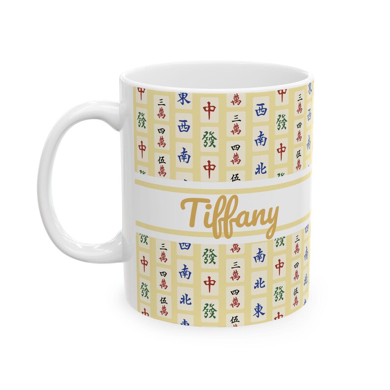 May include: White ceramic mug with a handle, featuring a design of Chinese characters and the name "Tiffany" in gold script. The mug has a cream-colored background with a pattern of red, green, blue, and black characters.