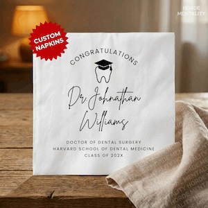 May include: White custom napkin with the text "CONGRATULATIONS" above a tooth wearing a graduation cap. Below, it reads "Dr. Johnathan Williams, DOCTOR OF DENTAL SURGERY, HARVARD SCHOOL OF DENTAL MEDICINE, CLASS OF 202X". A red starburst reads "CUSTOM NAPKINS".