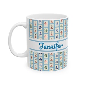 May include: White ceramic mug with a blue and white pattern of Mahjong tiles. The name "Jennifer" is written in blue script across the center. The mug has a white handle and a white interior.