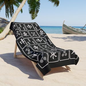 K&ouml;nnte beinhalten: Ein schwarz-wei&szlig;er Strandstuhl mit einem Mahjong-Kachelmuster. Der Stuhl steht auf einem wei&szlig;en Sandstrand mit Palmen und einem Boot im Hintergrund.