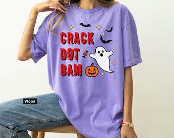 Puede incluir: Camiseta violeta con un diseño de Halloween. El diseño incluye las palabras "CRACK DOT BAM" en rojo, un fantasma blanco, una calabaza, murciélagos y estrellas. La camiseta es de estilo casual.