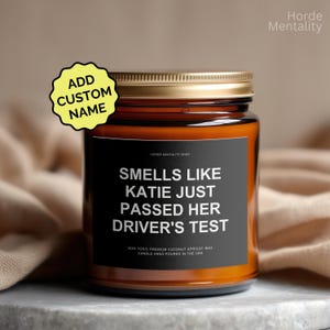 Könnte beinhalten: Duftkerze in einem Glas mit goldenem Deckel. Das schwarze Etikett lautet "Smells Like Katie Just Passed Her Driver's Test". Ein gelber Aufkleber sagt "Add Custom Name".