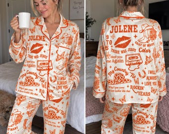 May include: A cream-colored pajama set featuring an orange graphic print of cowboy boots, hats, butterflies, cassette tapes, and lips. The text includes "Jolene," "9 to 5," "There Was Jesus," "Here You Come Again," "My Country 'Tis," and "I Will Always Love You."