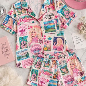Op de afbeelding: Een pyjamaset met een pyjamashirt met korte mouwen en knoopsluiting en een bijpassende short, voorzien van een kleurrijke collageprint van Dolly Parton, gitaren, vlinders, bloemen en postzegelafbeeldingen met een Tennessee-thema.
