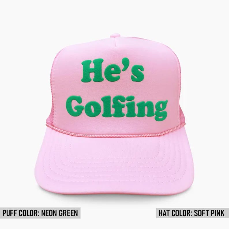 May include: A pink trucker hat with a neon green puff print that says "He's Golfing".