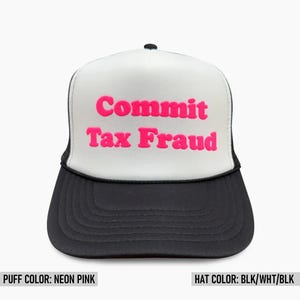 May include: A black and white trucker hat featuring the text Commit Tax Fraud in raised neon pink lettering. The cap has a white front panel, a black brim, and a black cord detail across the base of the front panel, with a structured foam crown.