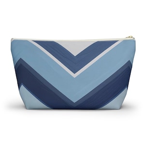 May include: A cosmetic bag with a chevron pattern in shades of blue and white. The bag has a zipper closure and a rectangular shape. The design features a series of angled stripes, creating a modern and stylish look.