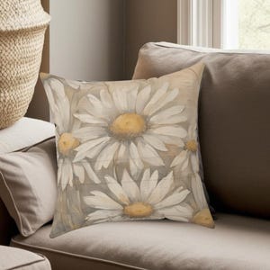 May include: A throw pillow with a floral design featuring white daisies with yellow centers on a beige background.