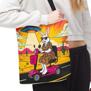 Può includere: Un coniglio bianco con occhiali da sole e un vestito a fantasia guida uno scooter di mobilità rosa in un paesaggio desertico con un UFO nel cielo.