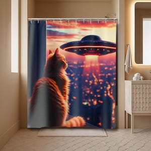 May include: Orange tabby cat looking out a window at a UFO hovering over a city at sunset. The shower curtain features a vibrant illustration with a red and orange sky, and city lights below.