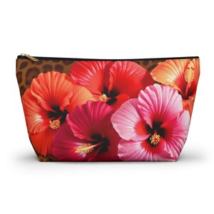 May include: A zippered cosmetic bag featuring a vibrant floral design of red, pink, and orange hibiscus flowers. The bag has a leopard print pattern at the top and a gold-colored zipper.