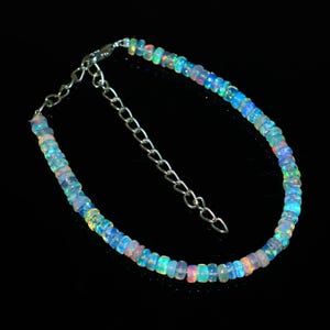 May include: A delicate bracelet featuring small, iridescent opal beads. The beads display a range of colours, including blue, green, and pink, strung together with a silver chain and clasp. The bracelet is designed to be adjustable.