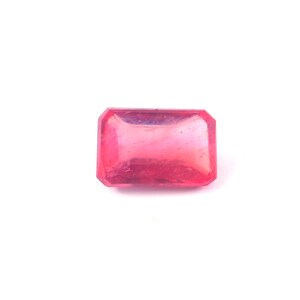 May include: A rectangular, faceted gemstone with a vibrant pink hue. The gem has a polished surface and a clear, translucent appearance. The gemstone is set against a plain white background.