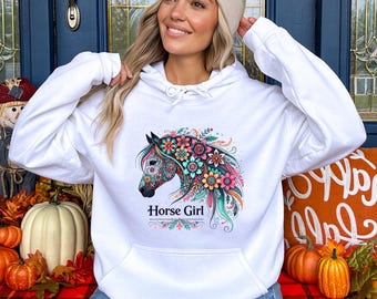 May include: White hoodie featuring a colorful horse head design with floral accents and the text "Horse Girl" in a script font. The horse design incorporates pink, blue, and green hues. The hoodie has a drawstring hood and a front pocket.
