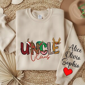 May include: Beige sweatshirt with the words "UNCLE Claus" in a festive design. The letter "U" is red plaid, "N" is leopard print, and "C" is green with a Christmas tree. The sleeve has the names "Alice, Olivia, Sophia" and a red heart.