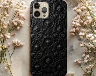 Könnte beinhalten: Schwarze Handyhülle mit einem erhabenen, verzierten Blumenmuster. Die Hülle hat eine matte Oberfläche und einen Kameraausschnitt mit drei Linsen. Der Hintergrund zeigt weiße Blumen und eine neutrale Oberfläche.