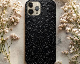 Könnte beinhalten: Schwarze Handyhülle mit geprägtem Blumenmuster. Die Hülle hat eine matte Oberfläche und ein erhabenes Design. Die Kameralinsen sind oben sichtbar. Weiße Blumen umgeben die Hülle.