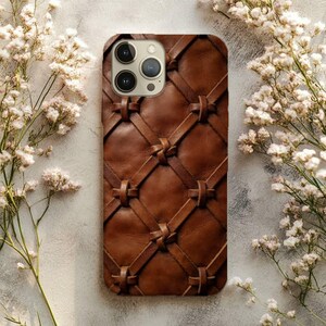 May include: A brown leather phone case featuring a woven lattice pattern with knotted intersections. The case has a rectangular cutout at the top left corner for a triple camera system, showcasing a smooth, textured surface with visible stitching.
