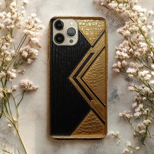 May include: A black and gold phone case with a geometric design. The case has a textured black centre panel with vertical lines, and gold accents with a crocodile skin texture. The case has a gold border and camera cutouts.