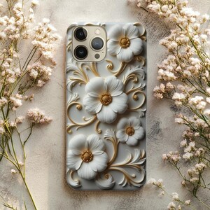 Puede incluir: Una funda de teléfono blanca con un diseño floral en 3D. La funda presenta flores blancas en relieve con centros y detalles dorados. El diseño incluye hojas y tallos dorados en espiral, creando un aspecto decorativo y elegante.