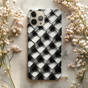 May include: A smartphone case with a geometric cube pattern in shades of silver and white. The case has a glossy finish and a camera module with three lenses. The background features white flowers.