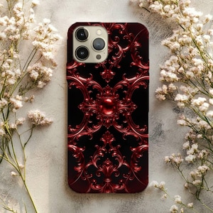 May include: A rectangular smartphone case featuring a deep black background with a symmetrical, raised, metallic red filigree pattern. The design includes intricate swirling scrollwork and a central circular orb element. The camera lens array is visible.