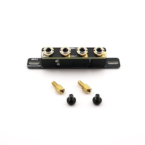 Peut inclure: Un module de composant noir doté de quatre prises d'entrée à bordure dorée disposées sur une rangée horizontale. L'unité comprend deux entretoises métalliques dorées et deux petites vis noires, avec le texte "MULT" et "MODULAR COMP" imprimé.