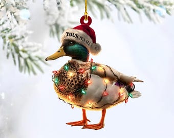 May include: A Christmas ornament shaped like a mallard duck, wearing a Santa hat with "YOUR NAME" printed on it. The duck is adorned with a string of colorful Christmas lights. The ornament hangs from a gold string.