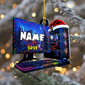 May include: A Christmas ornament shaped like a computer setup, including a monitor, keyboard, and PC tower. The monitor displays a winter scene with the text "NAME" and "2025". The PC tower is adorned with a Santa hat and string lights.