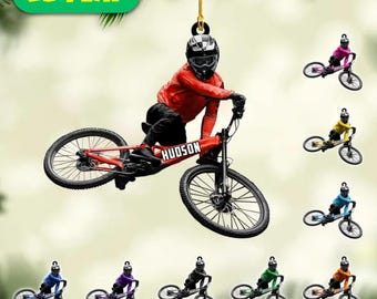 May include: A 2D flat ornament featuring a cyclist on a red bike with the name "HUDSON". The cyclist wears a red jacket and helmet. Additional ornaments in various colors are also shown. The text "2D FLAT" is in a green rectangle.