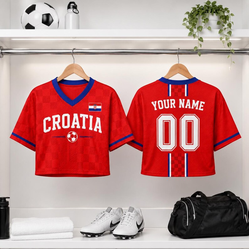 a pair of red Croatia soccer jerseys hanging on a rack, with the word "Croatia" printed on the front. The jerseys also have the text "Your Name" and the number "00" printed on the back. In addition to the jerseys, there are various sports equipment items such as a soccer ball, a water bottle, and a pair of sneakers.