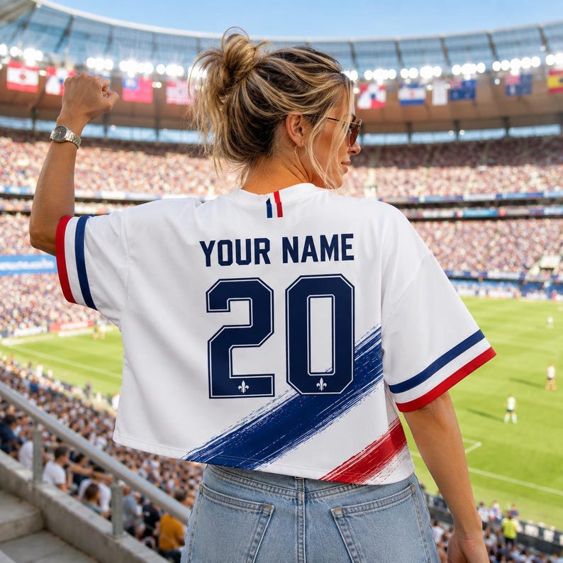 A woman wearing a white jersey with the number 20 and the text "YOUR NAME" on the back, standing in a crowded stadium.