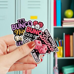 May include: A collection of colorful stickers with text and dice graphics. The stickers feature phrases like "It's Bunco Night" and "What Happens at Bunco". The dice are pink, white, and red.
