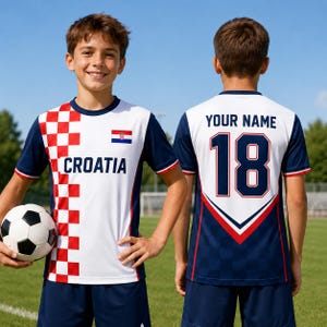 A young boy wearing a white and red soccer jersey with the word "Cratia" and the number 18, standing on a soccer field and holding a soccer ball.