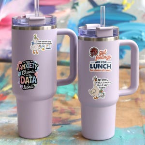 Puede incluir: Dos vasos t&eacute;rmicos aislados de color lavanda con asas y pajitas. Cada vaso tiene pegatinas humor&iacute;sticas. Uno dice "The Anxiety is Chronic but the Data is Iconic". El otro dice "Gut feelings are for lunch be data-driven."
