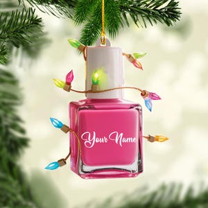 May include: A pink nail polish bottle Christmas ornament with the text "Your Name" in a cursive font. The ornament is decorated with colorful Christmas lights and hangs from a gold string.