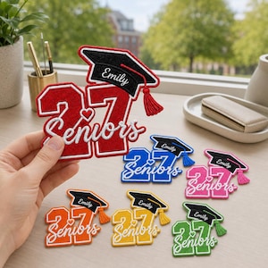 May include: A collection of embroidered patches featuring the number 27, the word Seniors in white script, and a black graduation cap with a tassel. The patches come in red, blue, pink, orange, yellow, and green, each personalized with the name Emily.