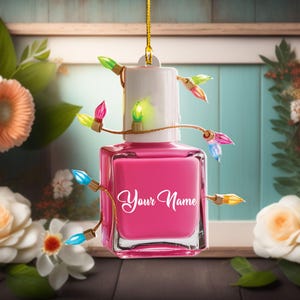 May include: A pink nail polish bottle-shaped ornament with a white cap, adorned with a string of colorful Christmas lights. The words "Your Name" are written on the bottle in a cursive font. The ornament hangs from a gold string.