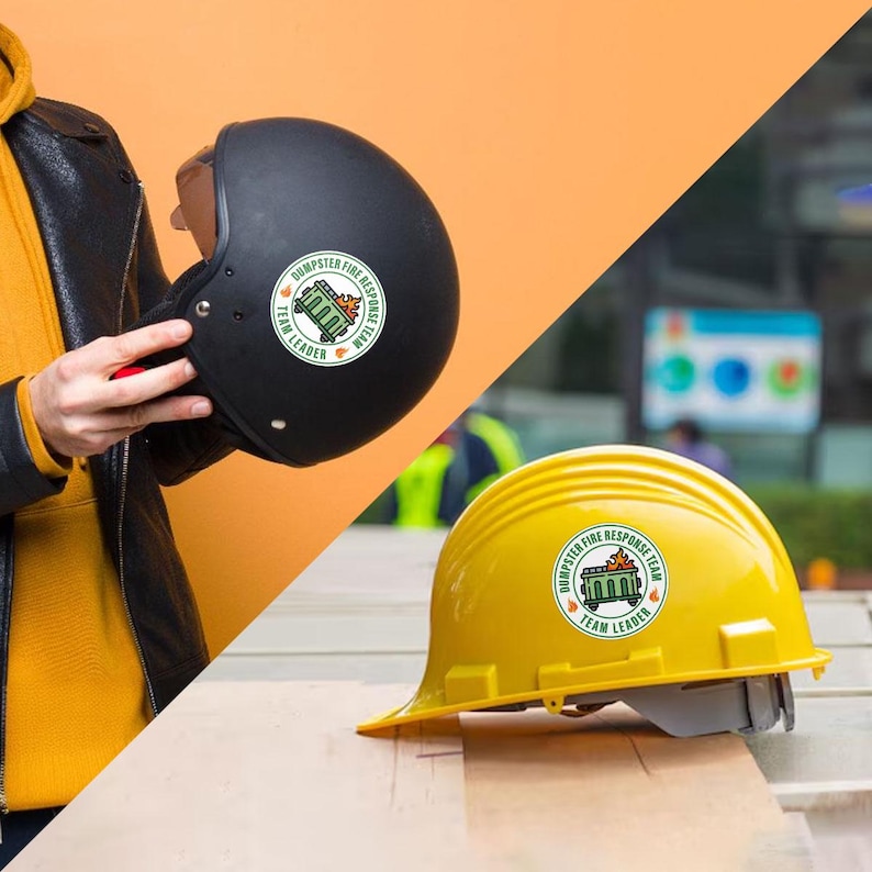 May include: A black helmet and a yellow hard hat, both with a circular sticker that reads "Dumpster Fire Response Team" and "Team Leader". The helmet is held by a person wearing a black jacket and yellow shirt.